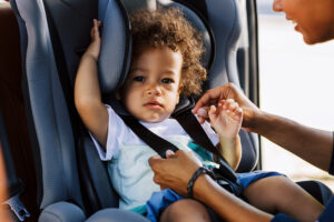 Taking Kids Out in Public. mom putting cute toddler in carseat for family outing