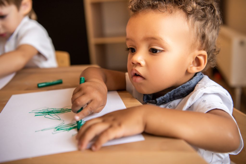 adorable african american boy drawing with green felt tip pen in kindergarten - SKIDamarink KIDs