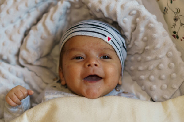 Little one month old baby lying in bed and smiling very happily Baby Concept - SKIDamarink KIDs infant first smile