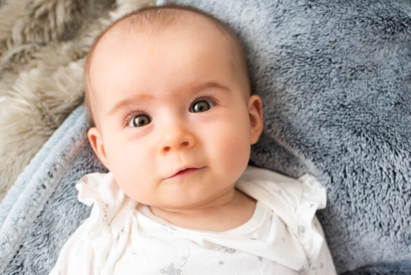 Portrait of baby with big eyes lie on back and looks up at camera - SKIDamarink KIDs