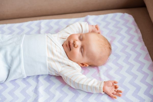 adorable newborn baby with closed eyes and raised hands lying on sofa - SKIDamarink KIDs adorable newborn baby with closed eyes and raised hands lying on sofa