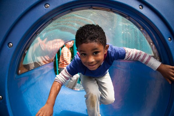 Boy bending forward emerging from playground tunnel - SKIDamarink KIDs Boy bending forward emerging from playground tunnel