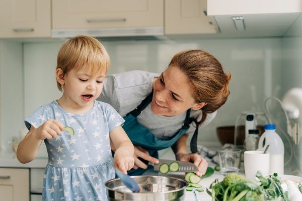 Funny toddler daughter helps mom cook in the home kitchen and eats vegetables - SKIDamarink KIDs Funny toddler daughter helps mom cook in the home kitchen and eats vegetables.
