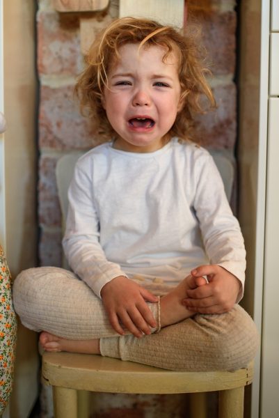 Portrait of unhappy small girl sitting indoors in kitchen at home, crying