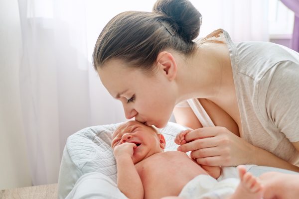 Young mom kissing crying newborn baby son - SKIDamarink KIDs responsive caregiving- Skidamarink Kids