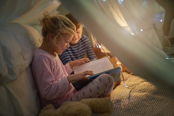 Cropped shot of siblings reading a story under a blanket fort at home - SKIDamarink KIDs Cropped shot of siblings reading a story under a blanket fort at home