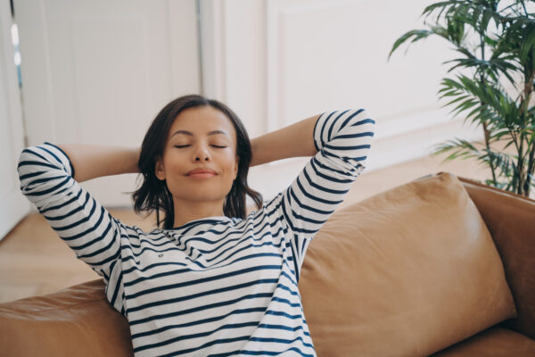 Female rests sitting on comfortable couch breathing fresh air at home Stress free wellness concept - SKIDamarink KIDs