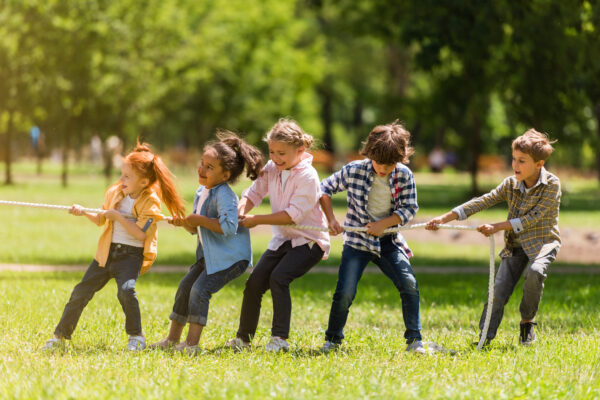 side view of adorable multiethnic kids pulling rope in park - SKIDamarink KIDs childhood development, children playing tug-o-war outside